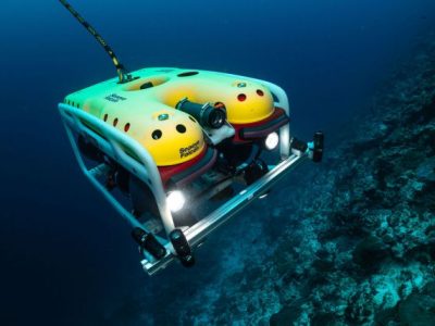 Robot submarino equipado con cámaras y luces LED realizando tareas de mapeo en un entorno subacuático, destacando su tecnología avanzada para monitorear infraestructura crítica como plataformas y puertos.