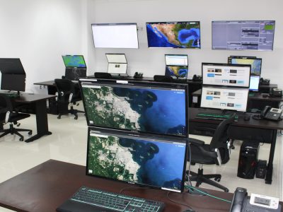 Centro de monitoreo con múltiples pantallas mostrando mapas satelitales y sistemas de vigilancia en tiempo real, diseñado para supervisión estratégica y análisis de datos.